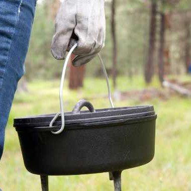 Person carrying a hot dutch oven in the outdoors.