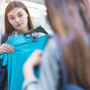 Woman holding up a shirt, looking in a mirror.