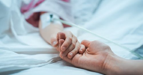 Recovering Little Child Lying in the Hospital Bed Sleeping, Mother Holds Her Hand Comforting. Focus on the Hands. Emotional Family Moment.