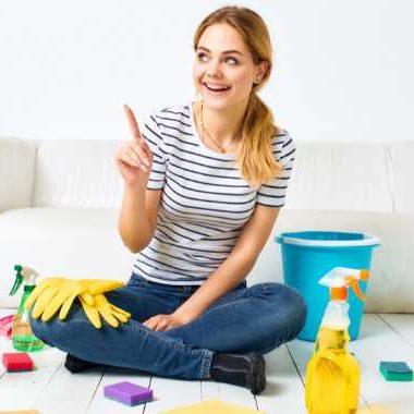 Happy woman sitting on the floor with cleaning supplies.