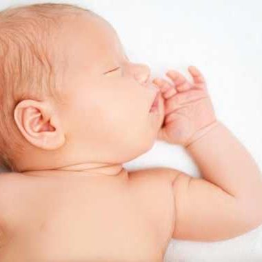 Newborn baby sleeping on back on white sheet