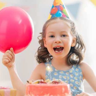 little girl smiling with pink balloon, party hat, and cake