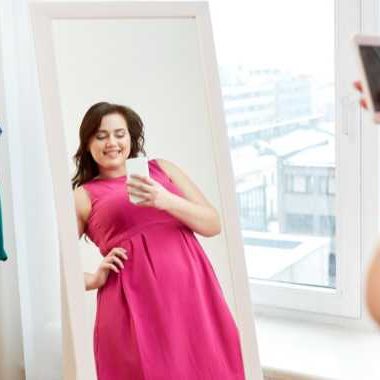 Woman in pink dress, looking in mirror, taking a selfie