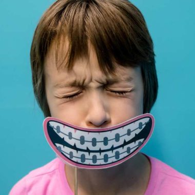 child with a picture of braces on teeth in front of his mouth