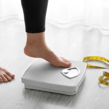 woman's feet stepping onto a scale with a tape measure nearby.