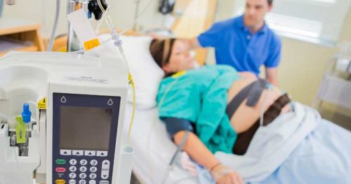 pregnant woman laying in bed with an epidural with an epidural pump in front.